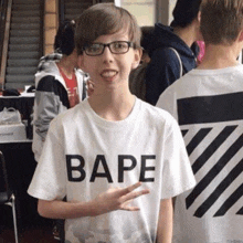 a young boy wearing glasses and a bape t-shirt is giving the peace sign .