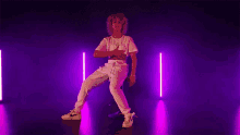 a woman is sitting on a stool in a dark room with purple lights behind her