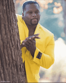 a man in a yellow suit is peeking around a tree