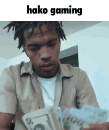 a man in a tan shirt is holding a bunch of money and says " hako gaming " on the bottom