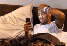 a man is laying in bed looking at a cell phone .