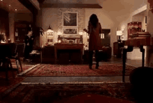 a woman in a red coat is standing in a living room with a rug .