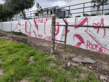 a chain link fence with graffiti on it next to a white wall .