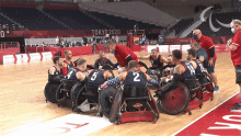 a group of men in wheelchairs are huddled together on a basketball court in front of a sign that says tokyo2020