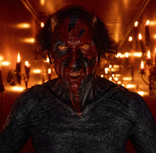 a man with red paint on his face is standing in front of a wall of candles