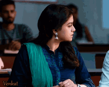 a woman wearing a blue shirt and green dupatta sits in a classroom with the word venkat on the bottom right