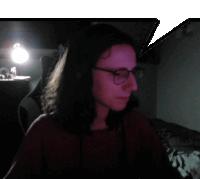 a woman wearing glasses and headphones looks at the camera in a dark room