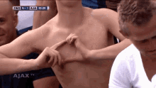 a shirtless man making a heart shape with his hands in front of ajax tv