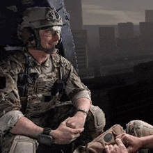 a soldier is sitting in a helicopter with a city in the background and talking to another soldier .