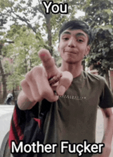 a young man is pointing at the camera while wearing a green shirt and a backpack .