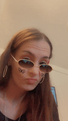 a woman wearing sunglasses and earrings has butterflies on her face