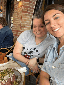 two women sitting at a table with one wearing a mickey shirt