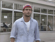 a man wearing a beanie and a blue shirt stands in front of a building with a sign that says american express