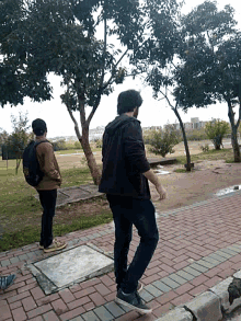 two men standing on a brick sidewalk one of whom is wearing a backpack that says ' a ' on it