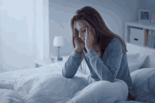 a woman in a blue shirt is sitting on a bed with her head in her hands