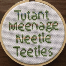 a cross stitch with the words `` mutant teenage mutant turtles '' written on it is in a hoop .