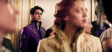 a man in a purple jacket and a woman in a white dress are standing next to each other in a room .