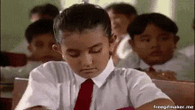 a boy in a school uniform and tie is sitting at a desk in a classroom with other students .