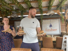 a man and a woman are holding plates of food in front of a sign that says ember