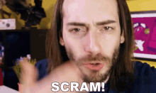 a man with long hair and a beard is pointing at the camera and saying scram