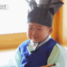 a little boy wearing a blue vest and a black hat is crying