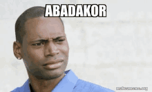 a man in a blue shirt is making a funny face with the words abadakor on his face .