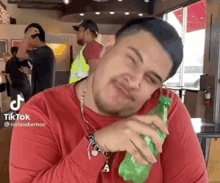 a man in a red shirt is holding a green bottle of soda in his hand .