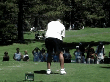 a man is swinging a golf club on a golf course in front of a green sign that says american cancer society