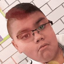 a boy wearing glasses is standing in front of a white brick wall with a bulletin board that says " a " on it