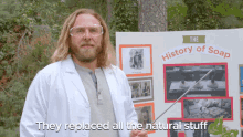 a man in a lab coat holds a stick in front of a sign that says the history of soap