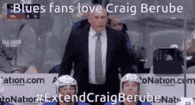 a man in a suit and tie stands in front of a group of hockey players and says blues fans love craig berube