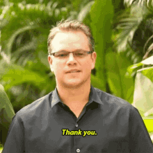 a man wearing glasses and a black shirt is standing in front of a green background and saying thank you .