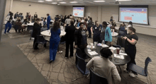 a large group of people are sitting at tables in a room with a projector screen .