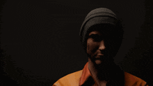 a man wearing a beanie and an orange shirt is in the dark