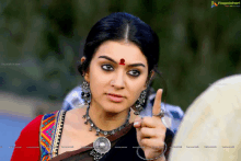 a woman with a red dot on her forehead is pointing at the camera