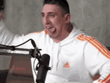 a man wearing a white adidas sweatshirt is sticking his tongue out in front of a microphone