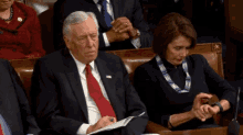 a man in a suit sits next to a woman in a black dress who is looking at her watch