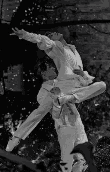 a black and white photo of two men dancing in the rain .