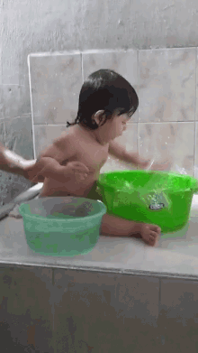 a baby is taking a bath in a bathtub next to a green bucket that says ' clorox ' on it