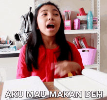 a girl sitting at a desk with her mouth open and the words aku mau makan deh