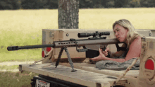 a woman sitting on the back of a truck with a sniper rifle and a license plate that says oklahoma