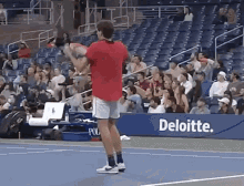 a man in a red shirt is holding a tennis racquet on a tennis court in front of a deloitte banner