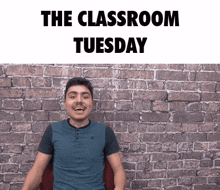 a man is smiling in front of a brick wall with the words " the classroom tuesday " above him