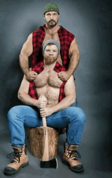 a man in a plaid shirt holds an axe while another man sits behind him