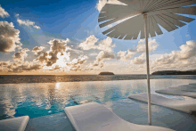 a swimming pool with a white umbrella in the foreground and the ocean in the background