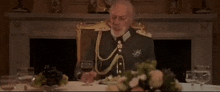 a man in a military uniform is sitting at a table with a glass of wine in his hand .