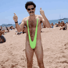 a man in a green slingshot giving a thumbs up on the beach