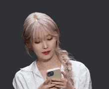 a woman in a white shirt holds a cell phone with a braided ponytail