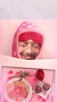 a man wearing a pink sleep mask is laying in bed with a tray of food and a rose