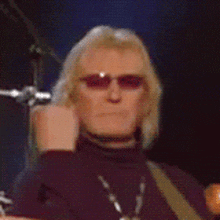 a man wearing sunglasses and a black turtleneck is playing drums